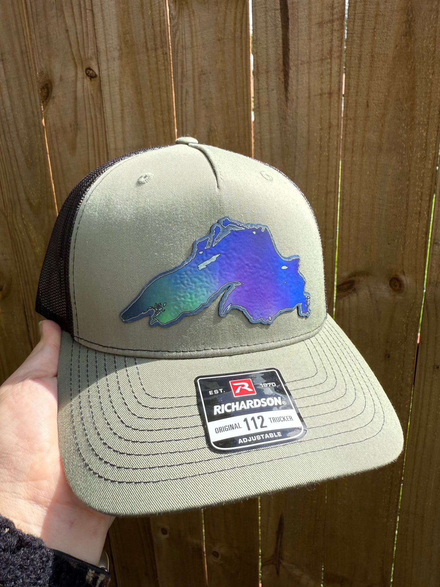 Beige cap with blue logo and brand label held against a wooden background