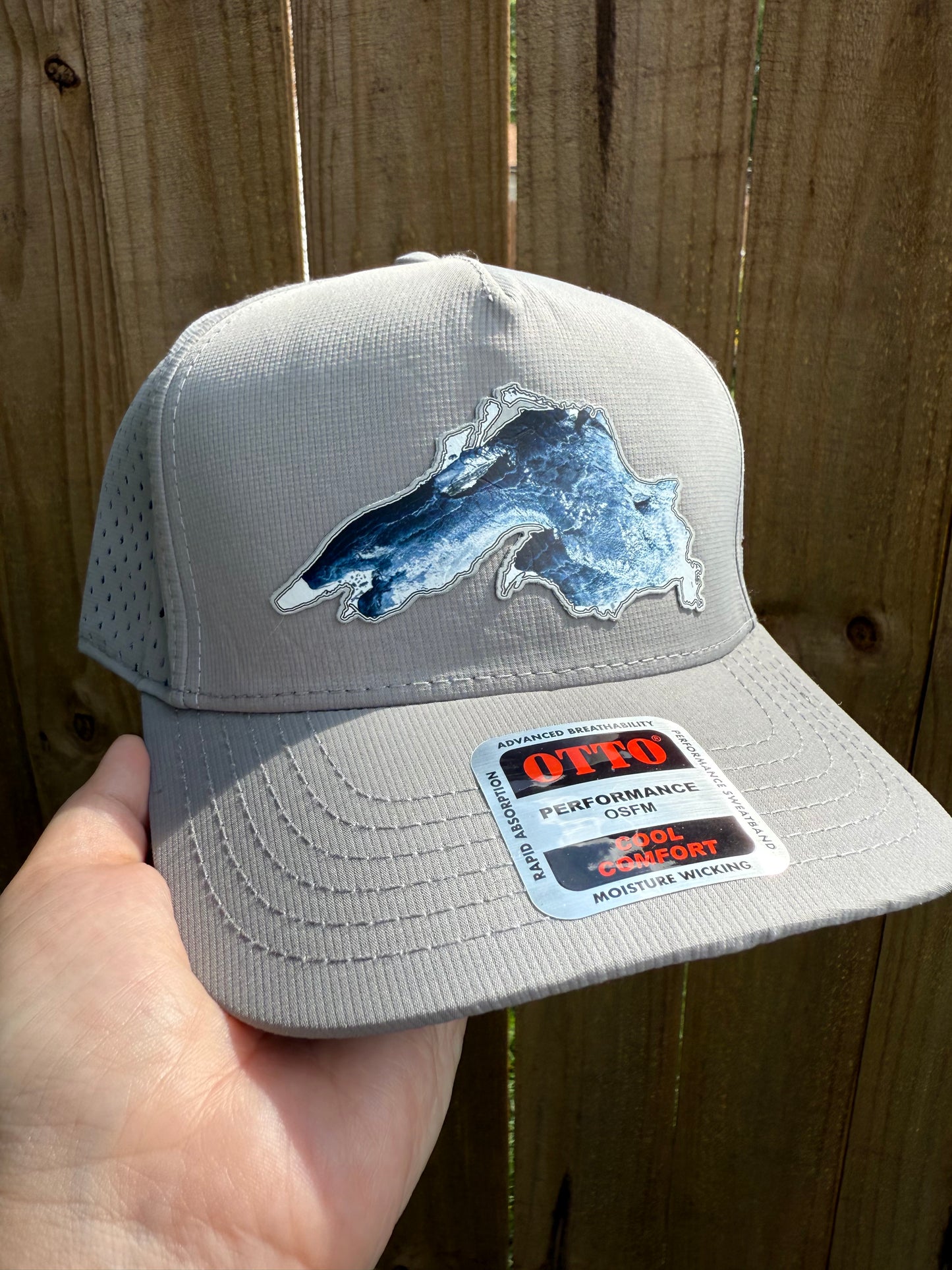 Gray cap with a blue graphic and a brand label held by a hand on a wooden surface
